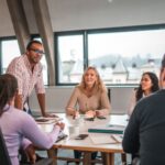 Rappresentazione della diversità e inclusione in azienda: un gruppo di colleghi, di ogni etnia, genere e capacità fisica, siede allo stesso tavolo di lavoro