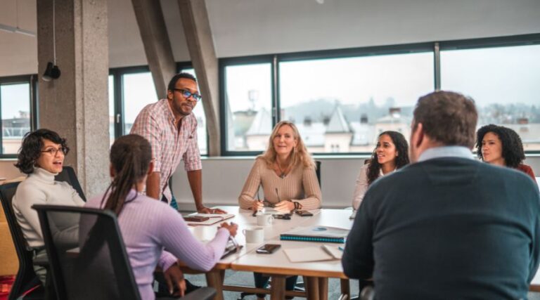 Rappresentazione della diversità e inclusione in azienda: un gruppo di colleghi, di ogni etnia, genere e capacità fisica, siede allo stesso tavolo di lavoro
