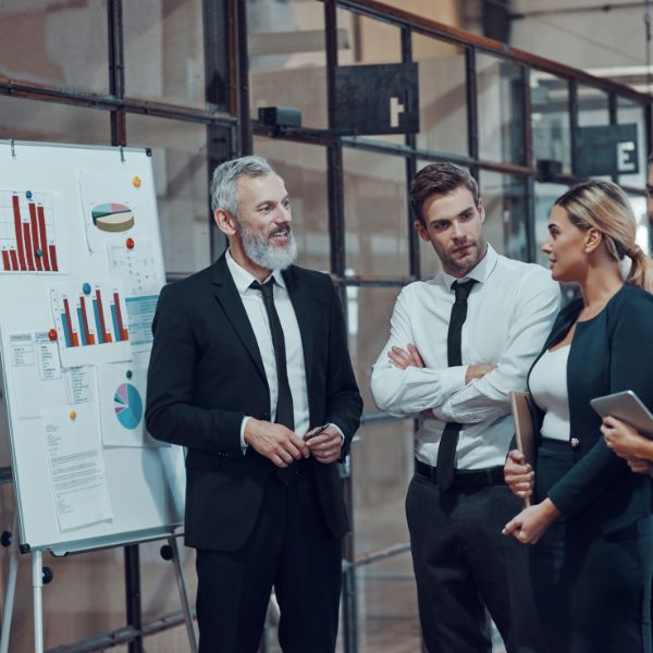Un trainer sta facendo un Managerial Training a due manager. Sono tutti in piedi di fronte a una presentazione su tabellone