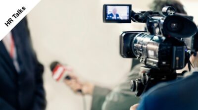 Un cameraman intervista la referente di Flamma Group, sullo sfondo