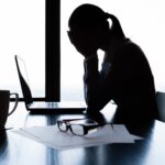 Collaboratrice seduta sulla scrivania, mentre si porta le mani verso il viso in segno di stress