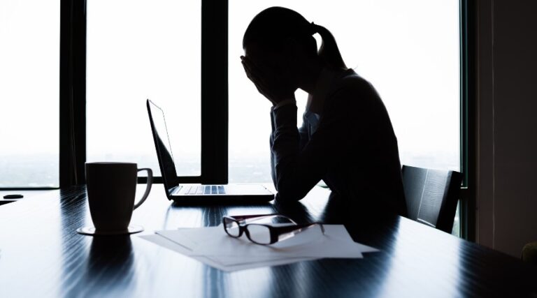 Collaboratrice seduta sulla scrivania, mentre si porta le mani verso il viso in segno di stress